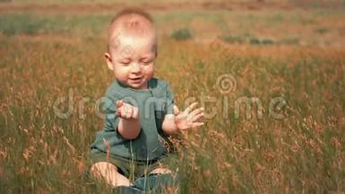 小男孩坐在草地上撕下青草。 夏天，快乐的小男孩在绿野上玩草。